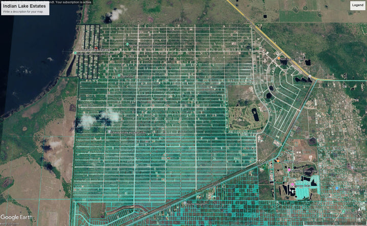 Satellite view of a large grid-like property or farm area with rows of greenhouses or agricultural plots, bordered by water on the left and urban land on the right. Google Earth interface elements are visible.