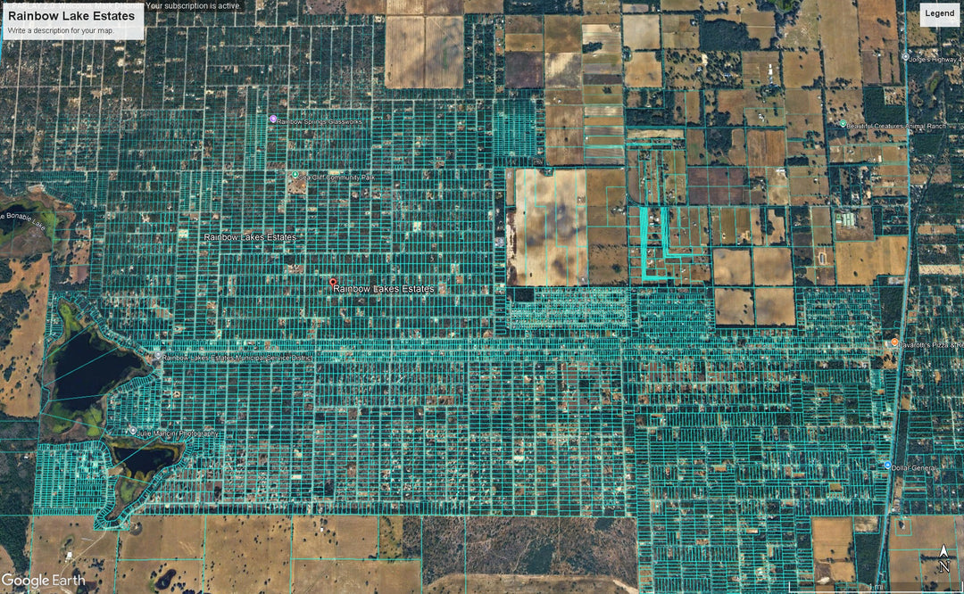 Aerial satellite view of a grid-like residential area labeled Rainbow Lake Estates, with many rectangular lots covered in bright green vegetation or fencing, surrounded by brown and tan farm fields.